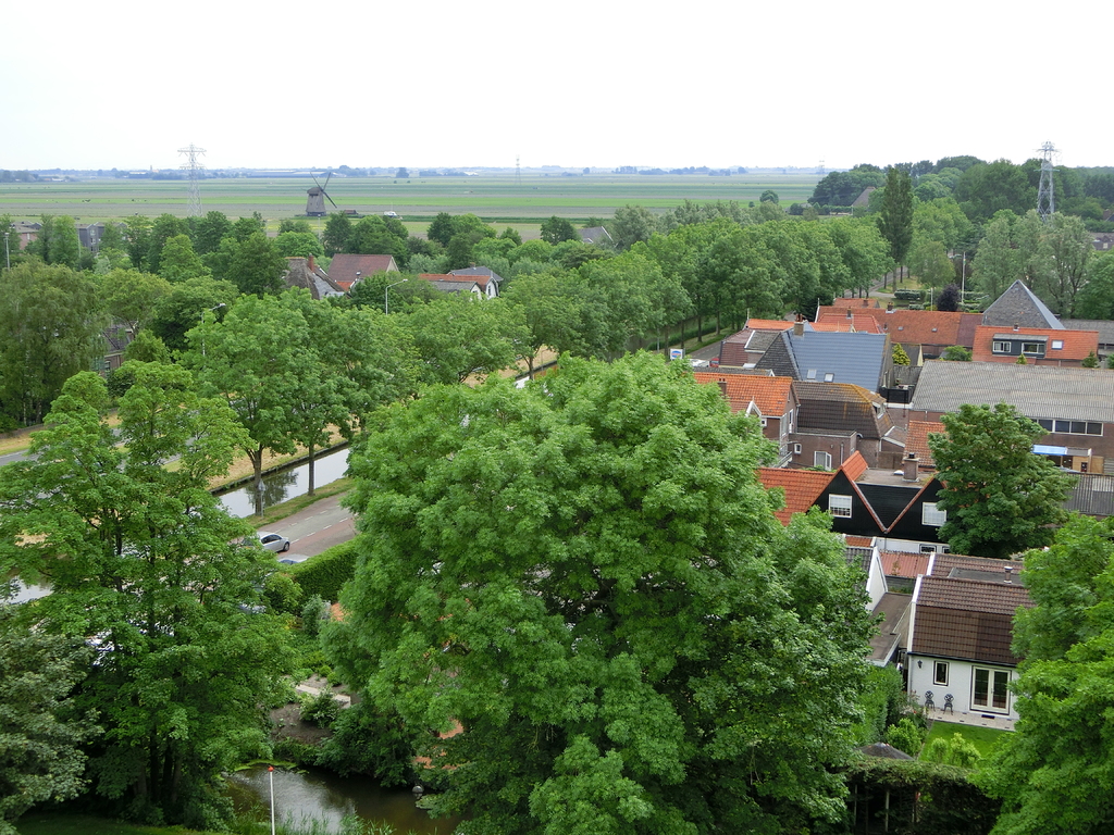 Eine Wohnsiedlung mit Häusern und Bäumen, Autos auf einer Straße und Türme mit einer Windmühle im Hintergrund.