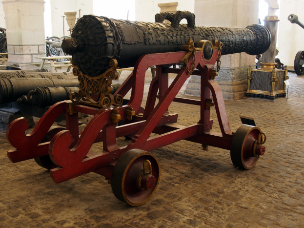 Ein altes Kanone in einem Museum ausgestellt, umgeben von anderen Kanonen und Säulen im Hintergrund.