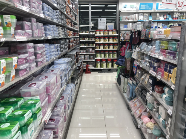 Ein unordentlicher chinesischer Supermarktgang mit Regalen voller Kartons, Flaschen, Tüten und anderen Artikeln, mit beleuchteten Schildern mit chinesischer Schrift, Deckenbeleuchtung und einem sichtbaren Feuerlöscher auf dem Boden.