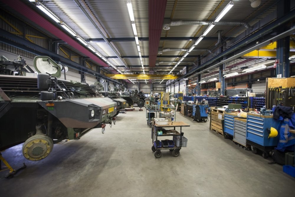 Großes Lager mit Maschinen, Fahrzeugen, Wagen, Holzboxen und Deckenbeleuchtung.