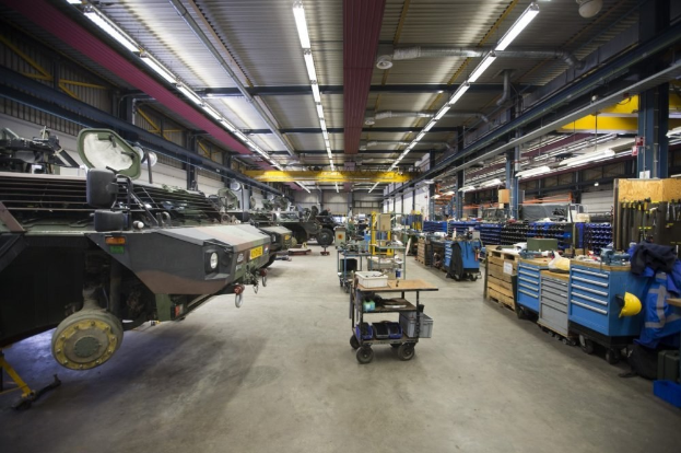 Großes Lager mit Maschinen, Fahrzeugen, Wagen, Holzboxen und Deckenbeleuchtung.