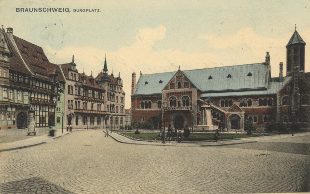 Eine alte Ansichtskarte, die den Burgplatz in Braunschweig, Deutschland, zeigt, mit einer Gruppe von Gebäuden, einer Statue auf einem Sockel, Menschen auf dem Boden, Pflanzen, Gras und einem bewölkten Himmel.