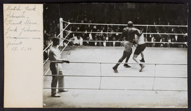 Schwarz-weiß-Foto von zwei Boxern im Ring, ein Schiedsrichter links und Zuschauer im Hintergrund, mit dem Text "Jack Johnson vs Frank Morgan" in der oberen linken Ecke.
