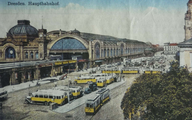 Eine sepiafarbene Postkarte des Dresdner Hauptbahnhofes mit einer belebten Straßenansicht mit Fahrzeugen, Fußgängern, Bäumen, Gebäuden und einem bewölkten Himmel.
