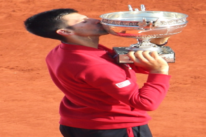 Novak Djokovic hält den French-Open-Pokal nach dem Sieg gegen Rafael Nadal im Finale der Herren-Einzel, steht mit einem triumphierenden Ausdruck da und küsst den Pokal.