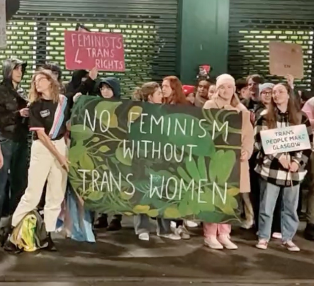 Eine Gruppe Von Menschen, Die Eine Banner Mit Der Aufschrift 'Kein Feminismus Ohne Trans Frauen' Und Schilder In Einer Öffentlichen Fläche Halten.