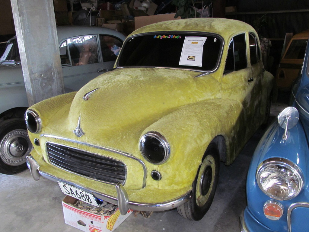 Mehrere Oldtimer vor einer Wand mit verschiedenen Zubehörteilen, mit einer Säule auf der linken Seite.
