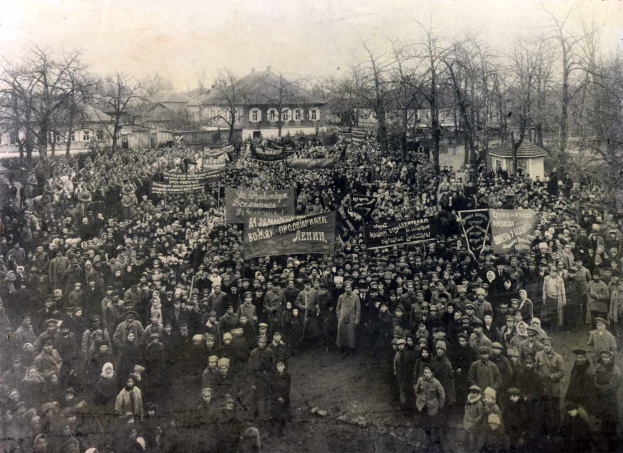 Eine große Menschenmenge mit Schildern steht vor einem Gebäude, mit Bäumen und anderen Gebäuden im Hintergrund, auf einem Schwarz-Weiß-Bild.