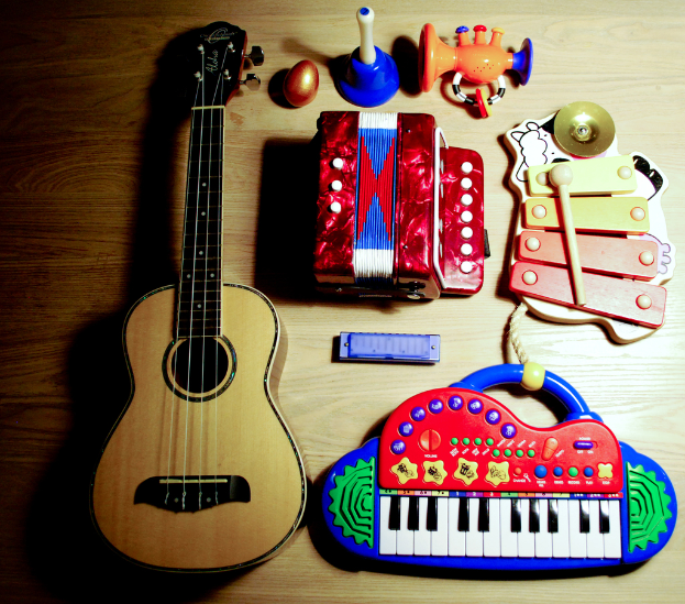 Ein Tisch mit verschiedenen Musikinstrumenten, darunter eine Gitarre, ein Xylophon, Harmonikas, ein Piano, ein Spielzeug, ein Plastikei und ein Horn.