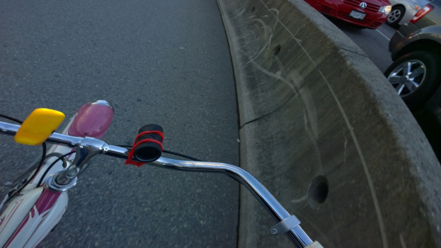 Ein Fahrradlenker befindet sich unten im Bild, mit Fahrzeugen, die auf der rechten Seite fahren, und einer Mittellinie.
