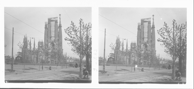Schwarzes und weißes Foto einer Straße in einer Stadt mit einer Kirche im Hintergrund, die eine Fassadenrestaurierung durchführt, umgeben von Bäumen, Masten und Menschen, unter einem sichtbaren Himmel.