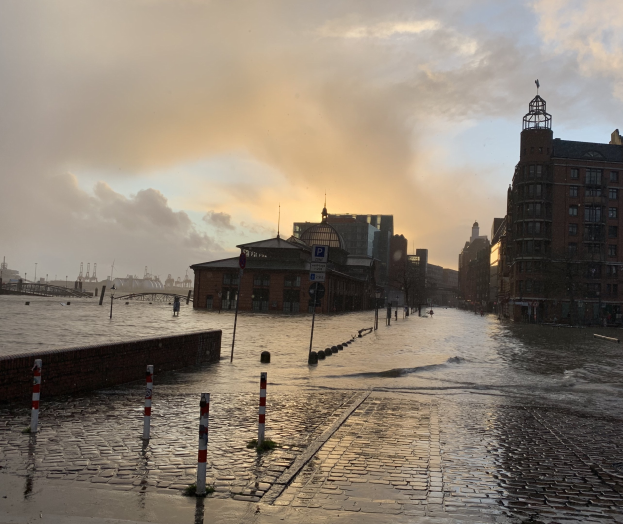 Überschwemmte Straße in Hamburg, Deutschland, mit Wasser, das die Straße, Pfosten, Schilder, Gebäude und eine Brücke bedeckt.