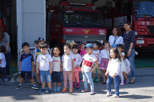 Eine Gruppe von Kindern vor mehreren Feuerlöschfahrzeugen auf einer Feuerwache, einige tragen Mützen.