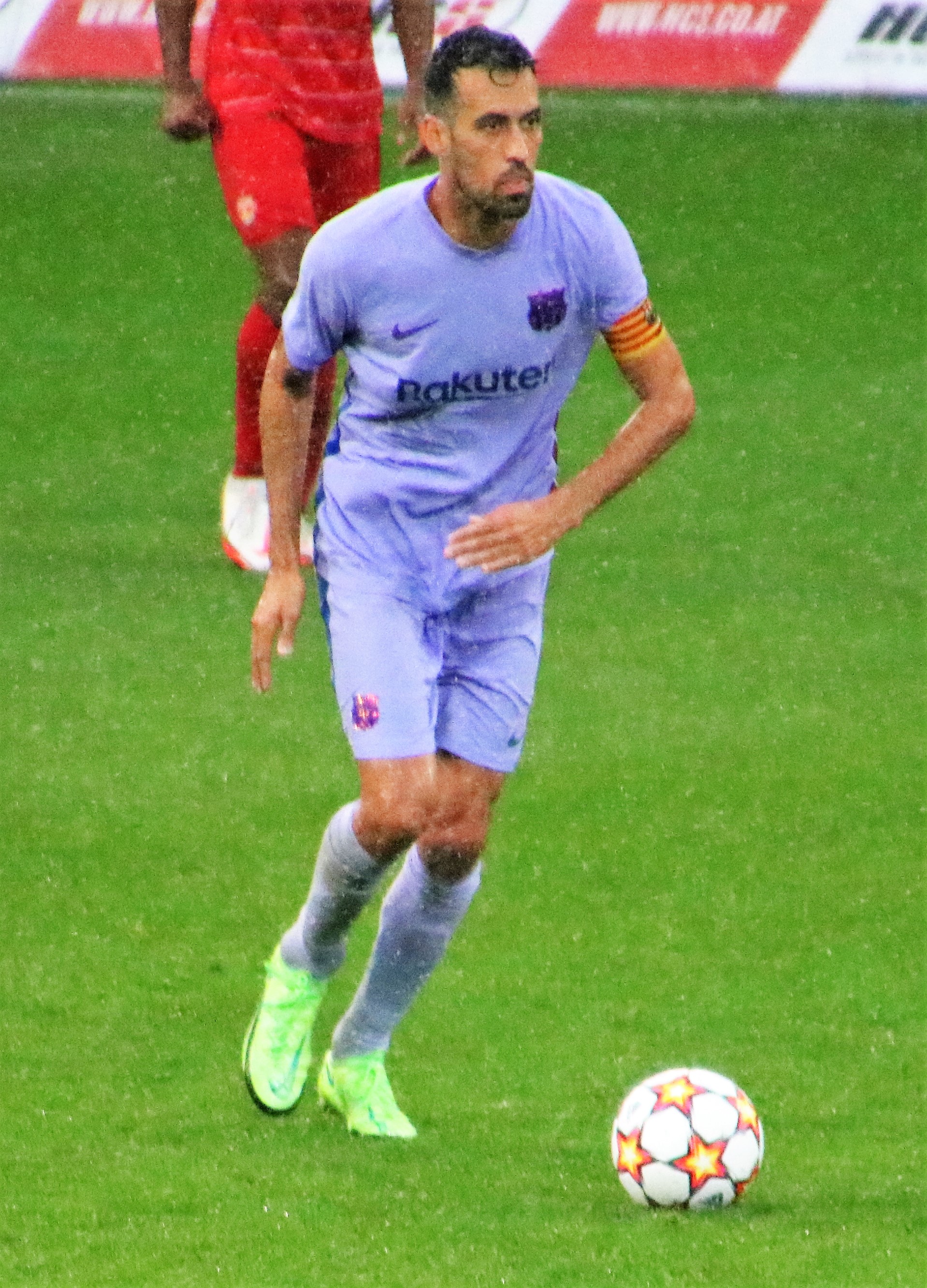 Ein Fußballspieler in Sportkleidung und -schuhen ist im Einsatz auf dem Feld, mit einer Tafel mit Text im Hintergrund sichtbar.