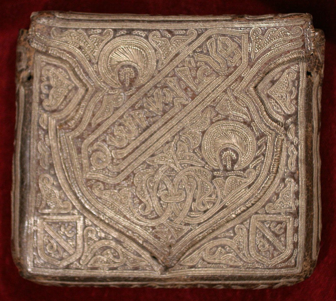 Ein goldbedecktes Buch mit detaillierten Designs auf einem roten Samt-Hintergrund.