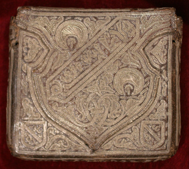 Ein goldbedecktes Buch mit detaillierten Designs auf einem roten Samt-Hintergrund.