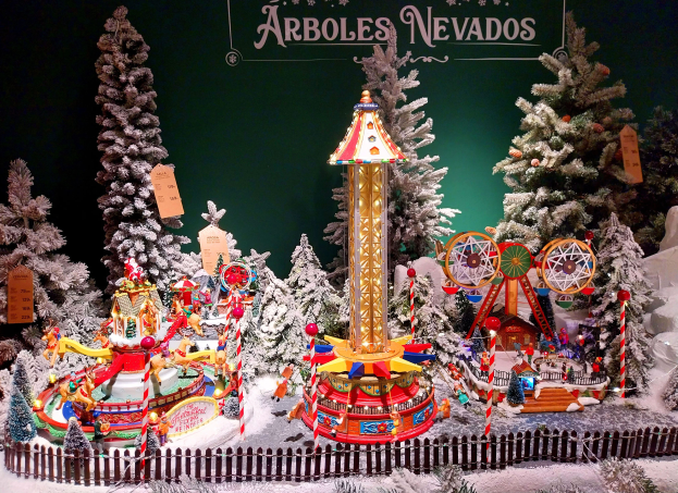 Ein festliches Weihnachtsdisplay auf dem Arboles Nevada Weihnachtsmarkt mit einem Karussell umgeben von schneebedeckten Tieren, einem Zaun, verschiedenen Spielzeugen und einer Tafel mit Text im Hintergrund.