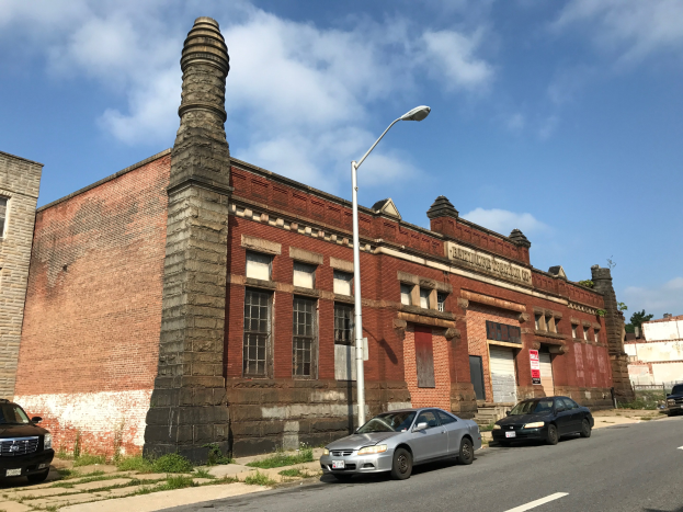Alter Backsteinbau mit seitlichem Schornstein, als ehemalige St. Louis Feuerwache bezeichnet, umgeben von Straßenlaternen, Lampen, Fahrzeugen, Schildern, Bäumen und einem bewölkten Himmel.