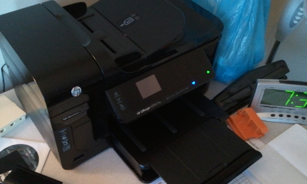 Ein digitaler Timer, ein HP-Drucker, eine blaue Polythenedecke, eine CD in ihrer Hülle, Papier und einige andere Gegenstände sind auf einem Tisch angeordnet.