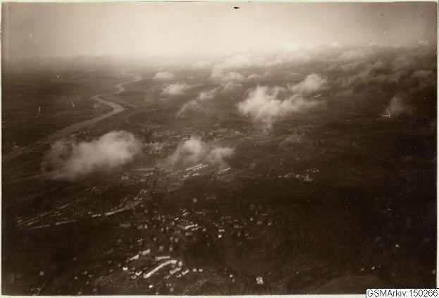 Eine Schwarz-Weiß-Aufnahme einer Stadt aus der Luft mit Gebäuden, Straßen und Wolken, mit Text am unteren Rand: 'Boeing B-17 Flying Fortress in Deutschland'.