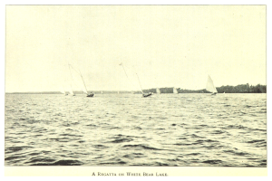 Regatta am Weißen Bärensee mit Booten auf dem Wasser, Bäumen im Hintergrund und Himmel darüber, einschließlich Text unten.