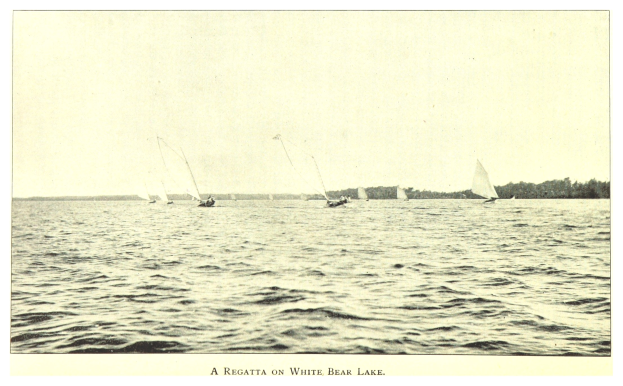 Regatta am Weißen Bärensee mit Booten auf dem Wasser, Bäumen im Hintergrund und Himmel darüber, einschließlich Text unten.