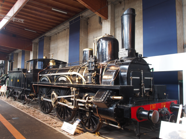 Alte Dampflokomotive in einem Museums Setting mit umgebenen Eisenbahnschienen, Informationsschildern und anderen Ausstellungen.