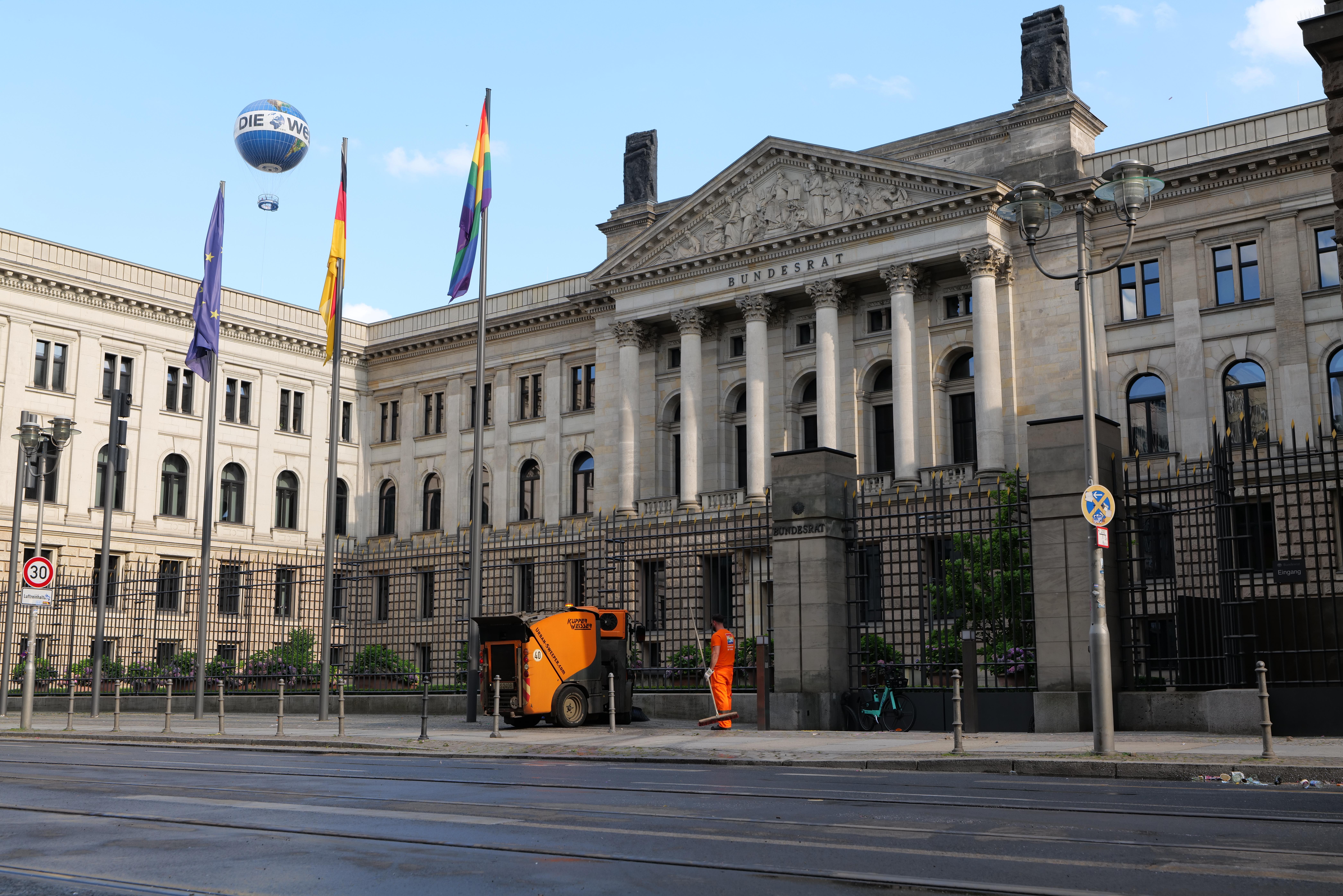 Das Reichstagsgebäude in Berlin, Deutschland, ein großes Gebäude mit zahlreichen Fenstern, umgeben von Straßenlaternen, Lichtern, Schildern, Fahrzeugen, Menschen, Flaggen, Gittern und Bäumen, unter einem bewölkten Himmel.