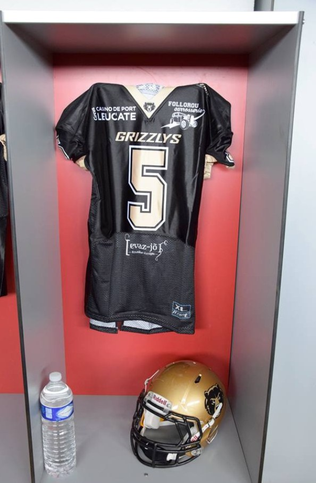 Ein Fuballtrikot und Helm hangen an einer Spindtür, mit einer Wasserflasche auf dem Regal darunter.