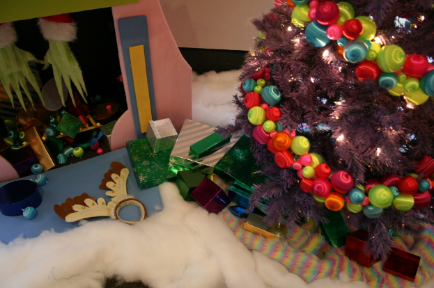 Drinnen, ein geschmückter Weihnachtsbaum rechts, Geschenkboxen und Dekorationen in der Mitte, eine Hütte mit Dekorationen oben links und Baumwolle und Wolle unten.
