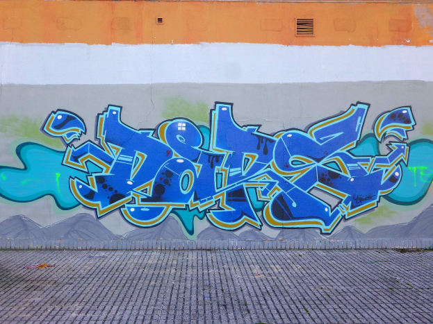 Eine Wand mit Graffiti-Kunst namens "album - graffitis dept 93 tom 030" vor einem Gebäude, mit dem Boden unten sichtbar.