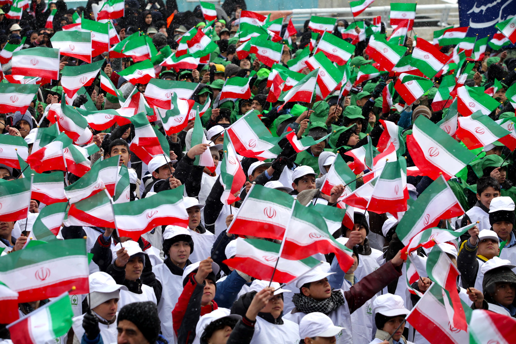 Eine große Menge Menschen mit iranischen Flaggen vor einem Gebäude, mit einer Fahne auf der rechten Seite und ein paar Menschen im Hintergrund.