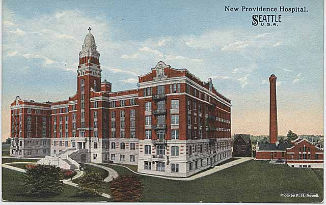 Eine Postkarte zeigt das New Providence Hospital in Seattle, Washington, mit einem großen Gebäude mit Fenstern, umgeben von Bäumen, Pflanzen, Gras und einem Weg, sowie einem Turm im Hintergrund und einem bewölkten Himmel, zusammen mit Text auf der Postkarte.
