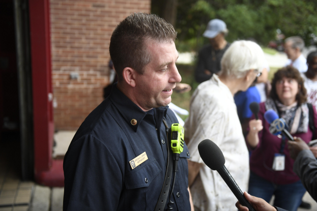 Ein Polizist in Uniform, der mit einer Gruppe von Menschen spricht, mit Bäumen und einem Gebäude im Hintergrund.