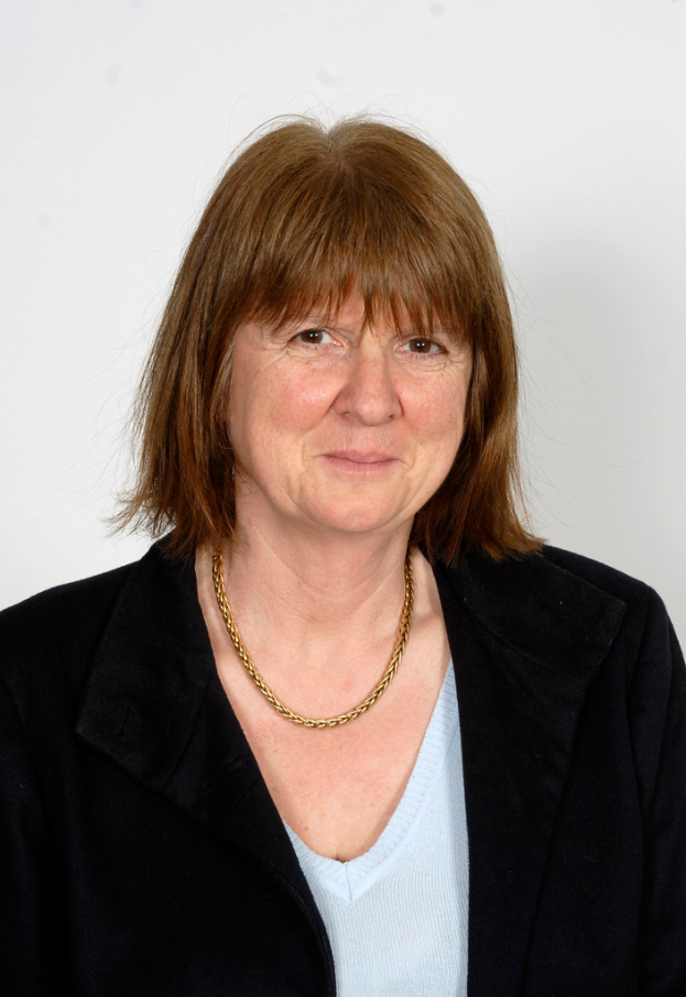 Eine Frau mit braunen Haaren, die eine schwarze Jacke und ein weißes T-Shirt trägt.