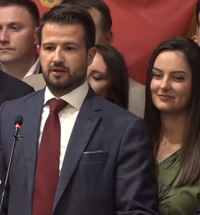 Ein Mann im Anzug und Krawatte steht an einem Rednerpult und hält eine Rede vor einer Menge mit einem Banner im Hintergrund, wahrscheinlich als Reaktion auf ein Regierungshandelsverbot für soziale Medien.