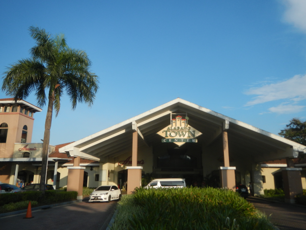 Der Eingang zu einem Resort mit Palmen vorne, umgeben von Gebäuden, Kraftfahrzeugen auf der Straße, Verkehrskegeln, Büschen, Bäumen und einem bewölkten Himmel im Hintergrund.