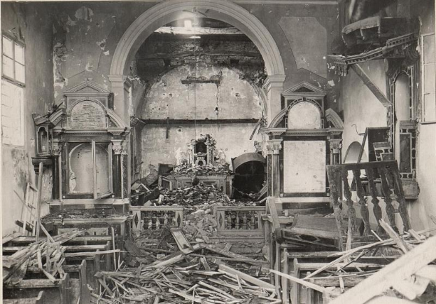 Ein altes Schwarz-Weiß-Foto eines feuerbeschädigten Kircheninneren mit verstreuten Holztrömmern und Fenstern auf beiden Seiten.