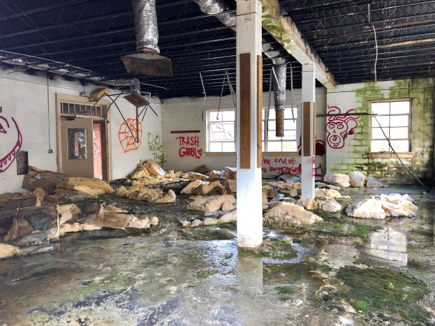 Ein verlassenes Gebäude mit Graffiti an den Wänden, Säulen und Fenstern, das eine Tür, ein Dach mit Metallstangen, Deckenleuchten und überflutete Böden zeigt, dient als Erinnerung an die Zerstörung durch den Hurrikan Sandy.
