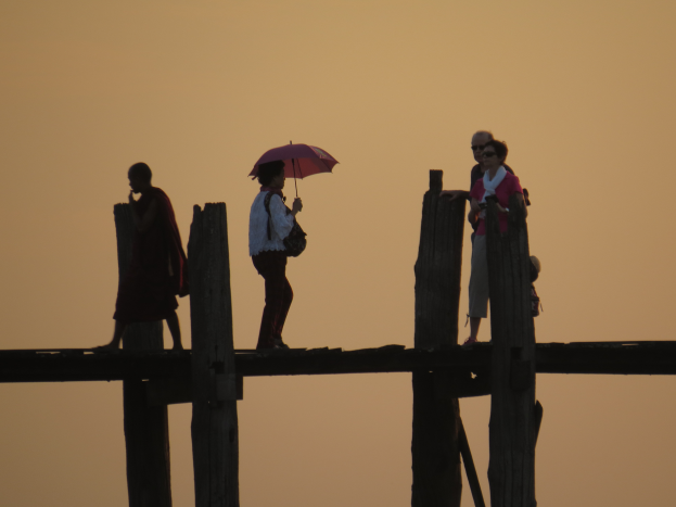 Eine hölzerne Brücke mit zwei Männern und zwei Frauen, die darauf gehen, vor einem Himmel im Hintergrund.