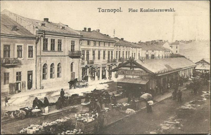 Schwarz-weiß-Foto eines vollen Marktes in Tarnopol, Polen, mit Menschen auf Karren und Gebäuden im Hintergrund.