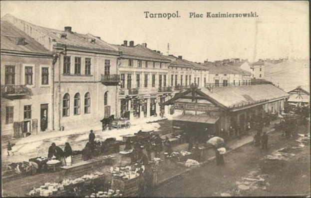 Schwarz-weiß-Foto eines vollen Marktes in Tarnopol, Polen, mit Menschen auf Karren und Gebäuden im Hintergrund.