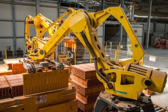 Großes Industriegebäude mit gestapelten Kisten, Kränen, Zaun, Pfählen und einer fernen Wand in einer automatisierten Produktionsumgebung.