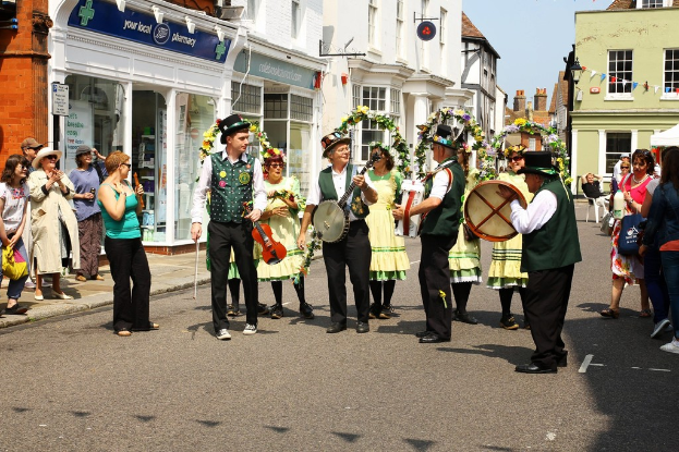 Eine Gruppe von Musikern, die Instrumente auf der Straße spielen, umgeben von ein paar Zuschauern und Gebäuden mit Geschäften und Schildern im Hintergrund.