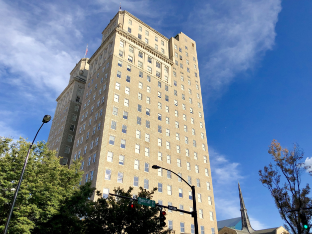 Historisches Marshall-Hotel-Gebäude mit vielen Fenstern, umgeben von Straßeninfrastruktur und Bäumen unter einem bewölkten Himmel.
