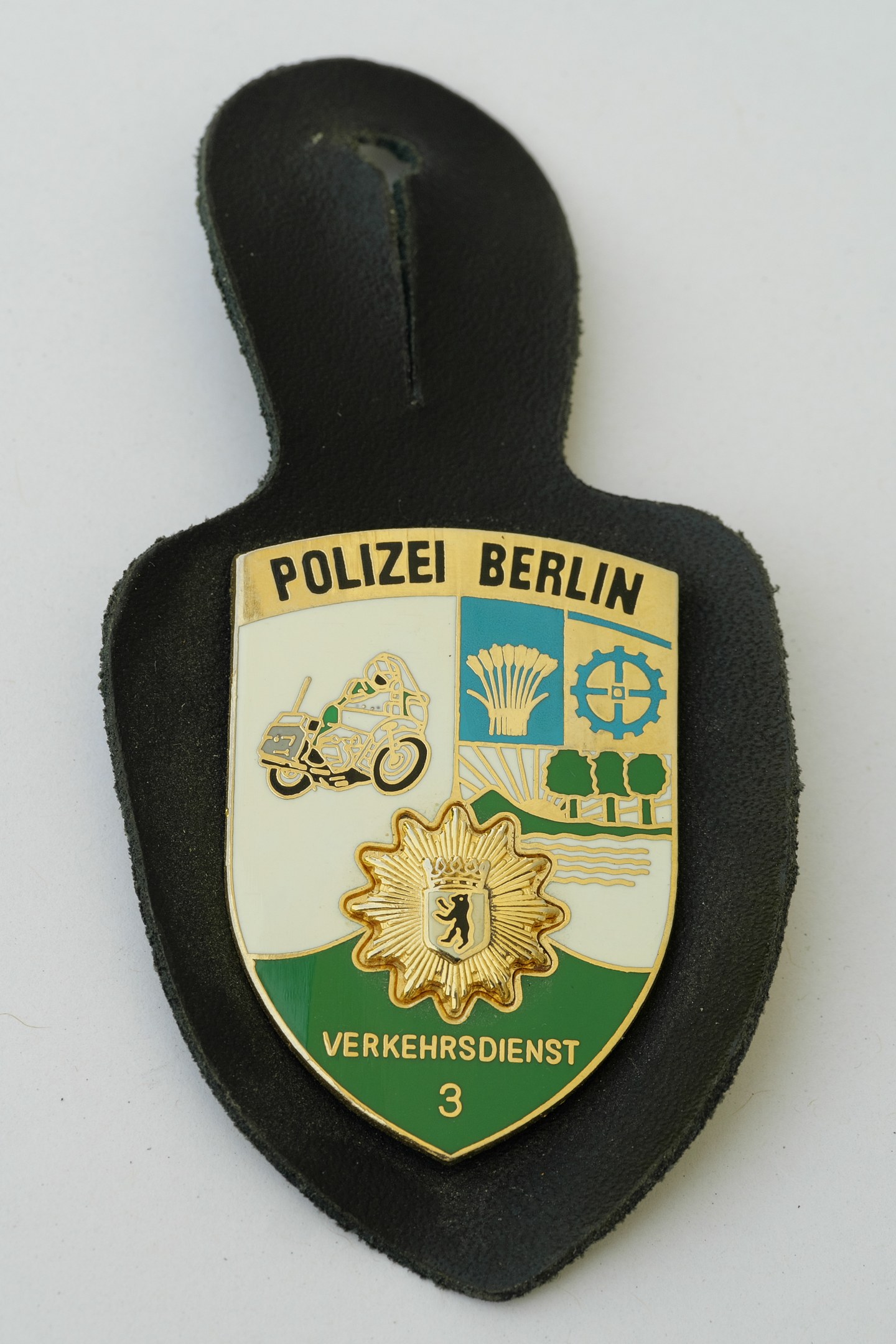 Ein schildförmiges Polizeibadge mit "Polizei Berlin" in schwarzer fetter Schrift, das ein weißes Stern auf blauem Hintergrund und einen weißen Rand hat und auf einer Oberfläche liegt.