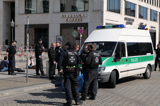 Eine Gruppe von Polizeibeamten steht vor einem Starbucks-Café, rechts ein Van und links ein paar Menschen, vor einem Gebäude, einem Schild, einem Laternenmast und einem Zaun.
