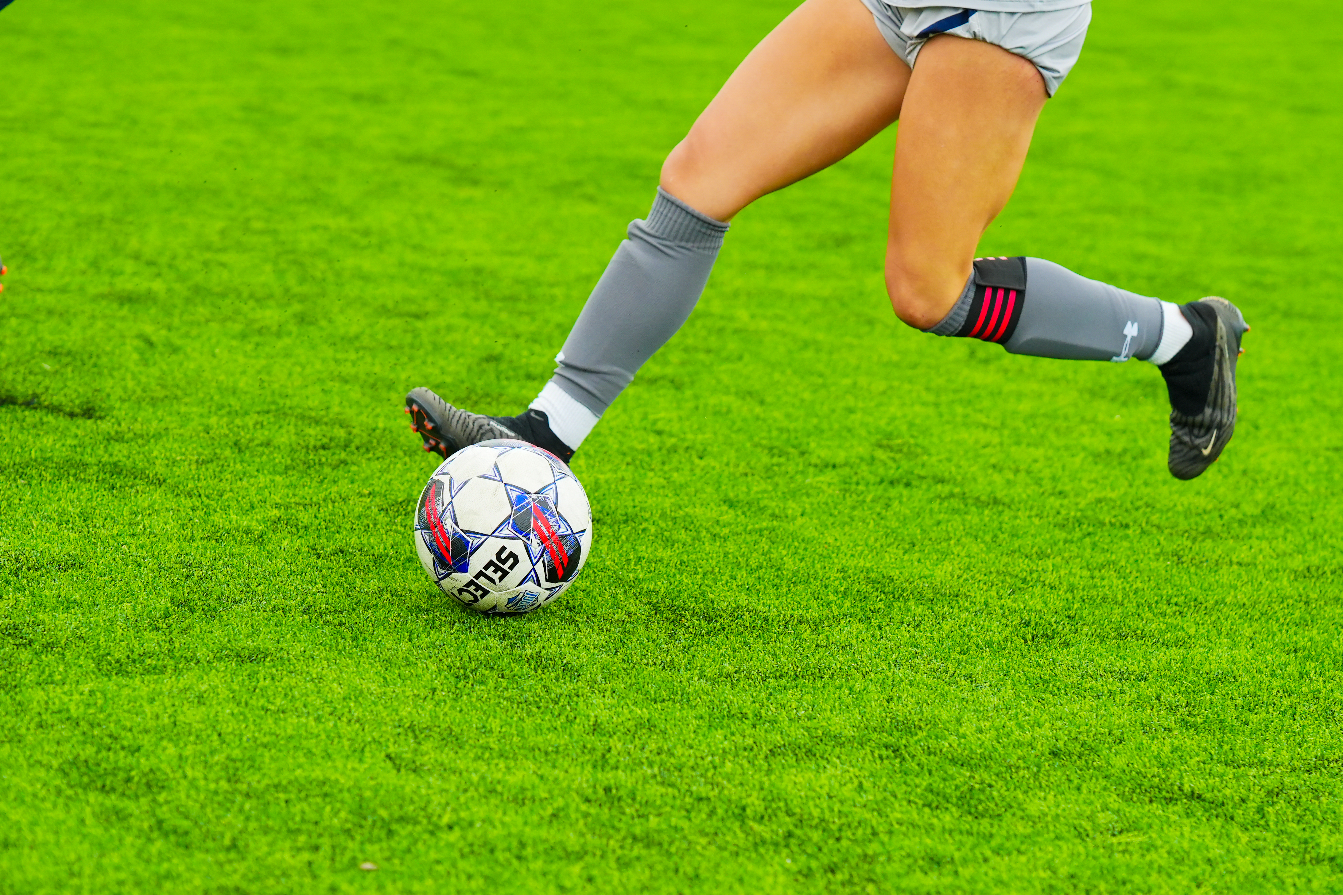 Eine Frau in Sportbekleidung und -schuhen kickt einen Fußball auf einem saftig grünen Feld, was darauf hindeutet, dass sie eine professionelle Fußballspielerin ist.