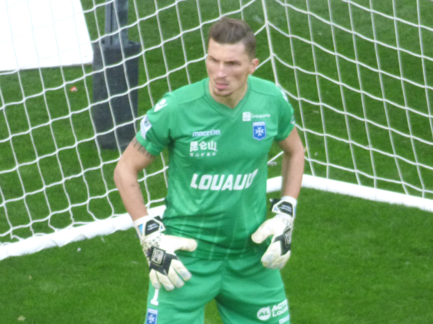 Ein Torwart in grüner Uniform steht vor einem Fußballtor auf saftigem Grün, trägt Handschuhe.