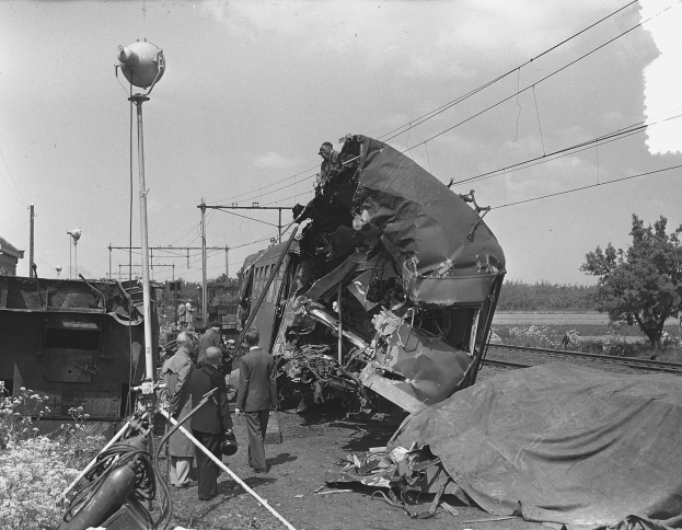 Ein Schwarz-Weiß-Foto eines Zuges, der auf der Seite der Straße gegen einen Pfahl geprallt ist, mit einigen Menschen um das Wrack herum und Bäumen, Pfählen, Drähten und dem Himmel im Hintergrund.